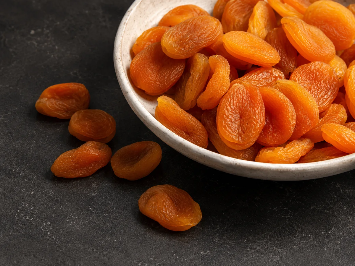 Golden Turkish dried apricots in a white bowl on a dark background